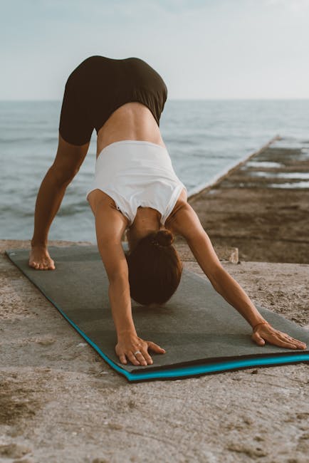 Person on a yoga mat stretching gently, seen from the back in a calm setting.